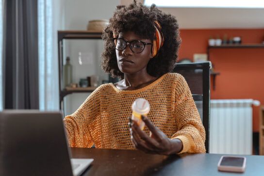 Adult female sitting in front of a laptop with a pill bottle in her hand possibly looking for information on what happens if you take Keppra and don't have epilepsy