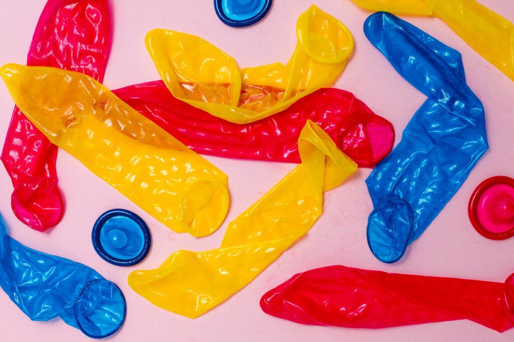 Yellow, blue, and pink condoms scattered across a surface to depict types of birth control.