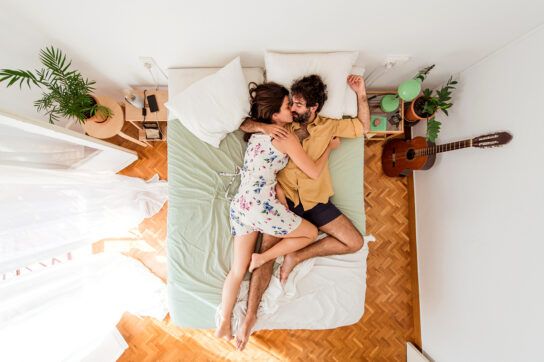 A young couple embracing in bed, wondering about using NuvaRing vs. IUDs as contraception.
