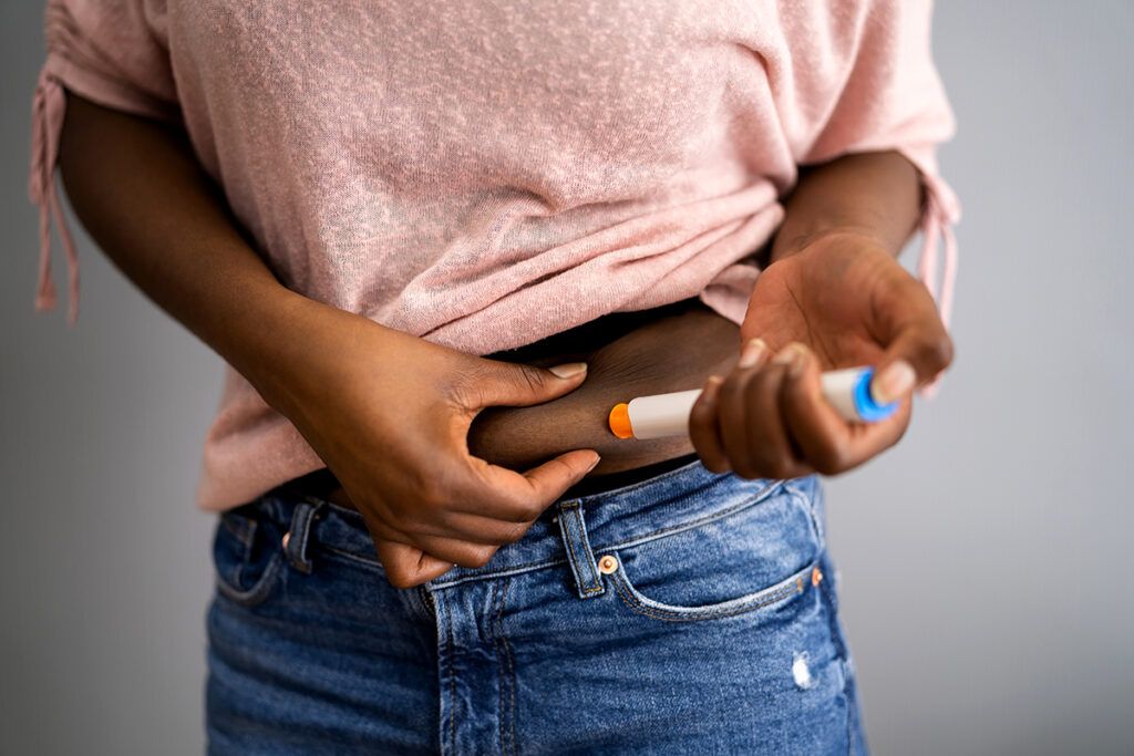 Person injecting an epipen in to their lower stomach to depict epipen coupons.