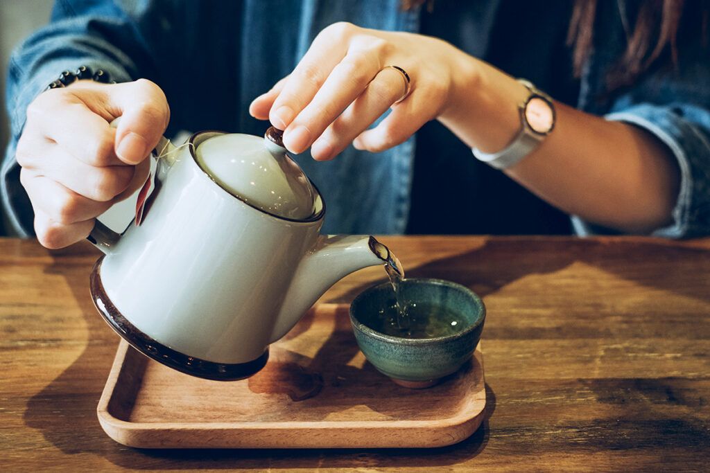 A person using a teapot to pour green tea into a cup, to depict OTC options for high cholesterol.