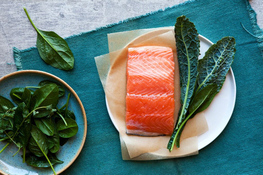 Two plates of leafy greens, one with a piece of salmon as an example of foods to focus on rather than what should I avoid while taking lisinopril