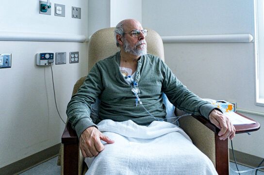 Older male sitting in a hospital chair receiving treatment to depict signs that chemotherapy is working.