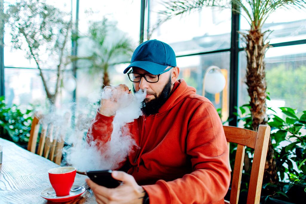 Male sitting at a table and vaping to depict whether vaping can cause high blood pressure.