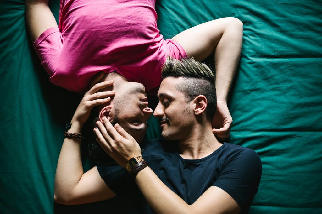 A young couple lying on a bed, holding each other's faces. They may be considering whether low testosterone causes erectile dysfunction.