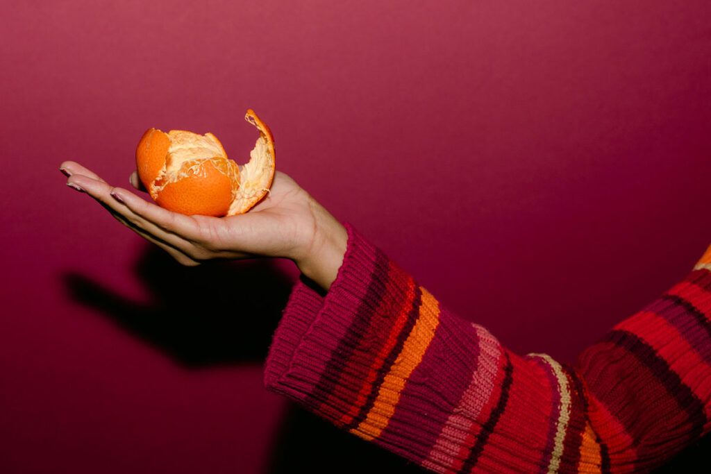 Person holding a peeled orange to depict signs of breast cancer.