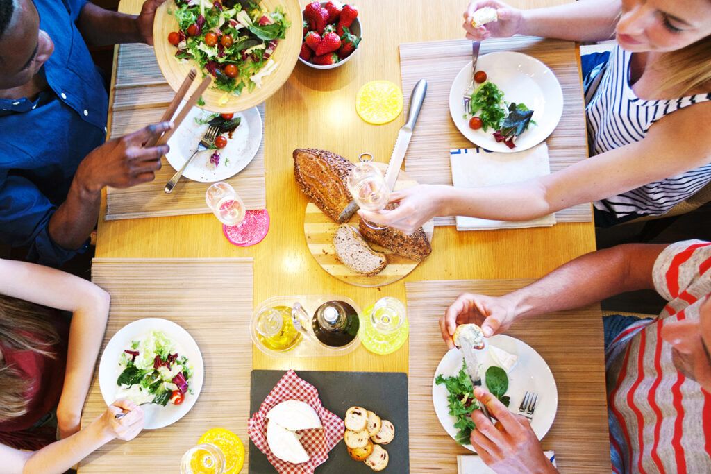 Overhead view of a dinner table with salad, bread, and cheese, and peoples arms reaching out to serve food possibly after researching foods for diabetes and how long it takes for Januvia to work