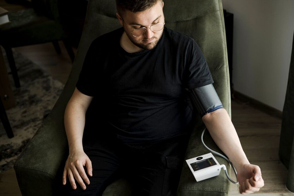 Adult male sitting in an armchair using an at home blood pressure monitor after wondering does Prozac raise blood pressure 