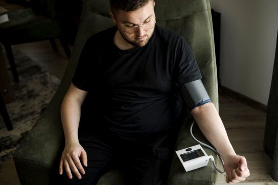 Adult male sitting in an armchair using an at home blood pressure monitor after wondering does Prozac raise blood pressure