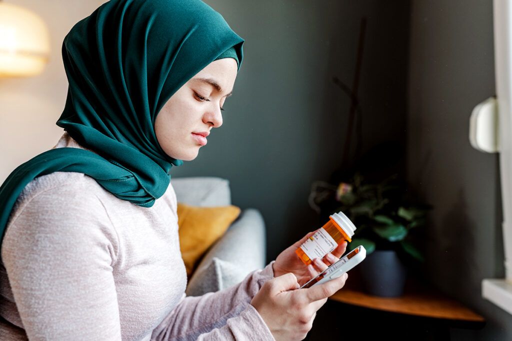 A young adult looking at a pill bottle and checking on her phone Mydayis vs. Adderall.