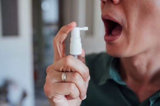 Adult male with an open mouth and holding a spray bottle about to spray a medication into her mouth which could be nitroglycerine for angina