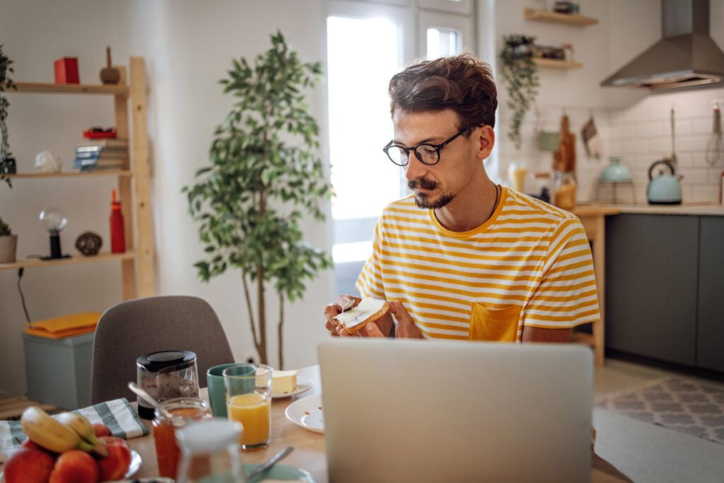 An adult eating breakfast in front of a laptop to avoid taking metoprolol on an empty stomach.