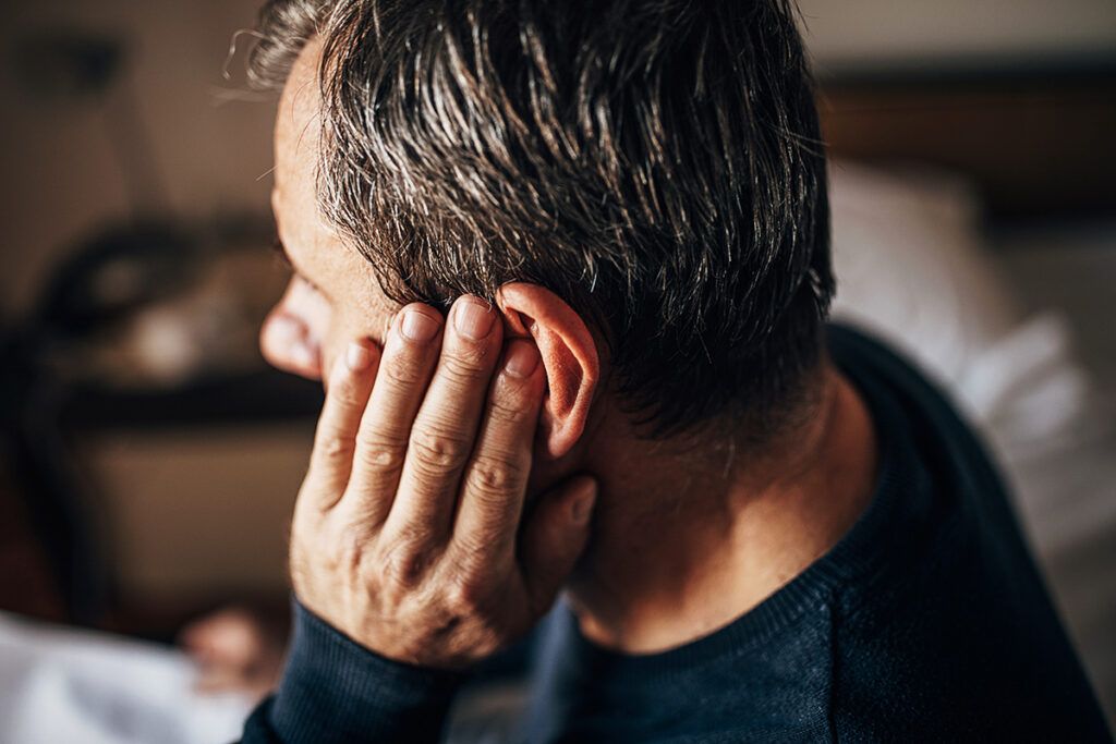 Side view of an adult male holding their left ear and possibly wondering about home remedies for ear infections in adults