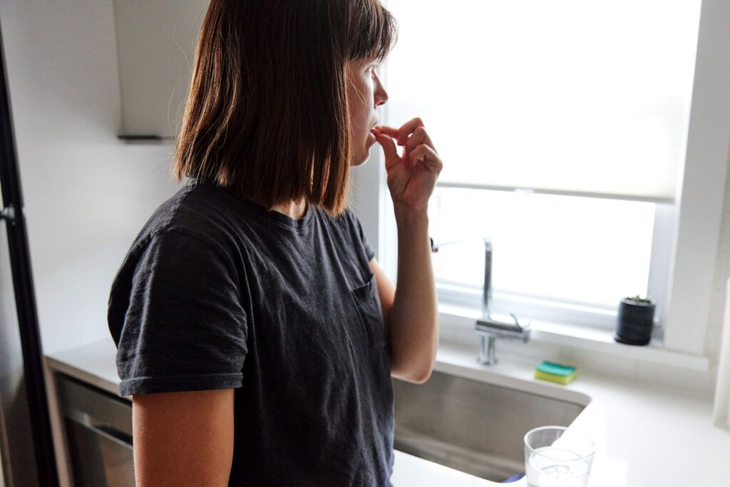 Person standing in their kitchen taking a pill to depict the risks of taking antibiotics when you don't need them.