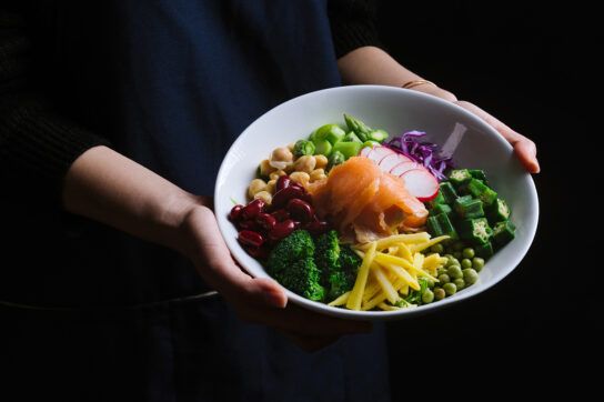 A pair of hands holding a bowl filled with a colorful salad, which is a helpful food for rheumatoid arthritis