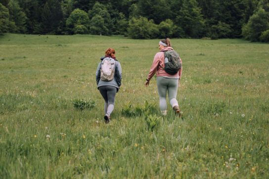 Two adults hiking through a field together, shown from behind.