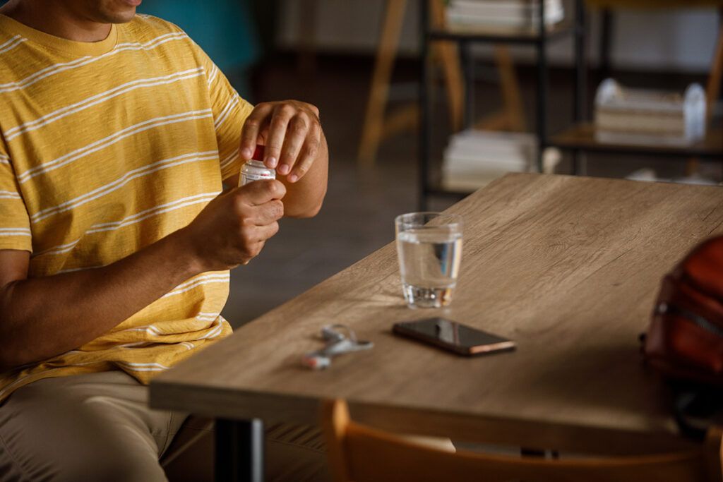 A young male taking erectile dysfunction medication sitting at a table with a glass of water on it.