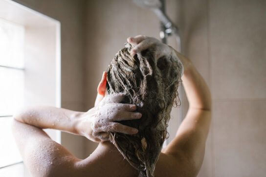 Woman in shower washing hair with shampoo lather