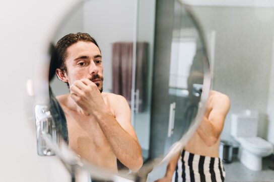 A person looking in a bathroom mirror and touching their lip, perhaps because of an incoming cold sore.