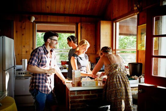 A group of adults working together in a kitchen with sunlight coming in.