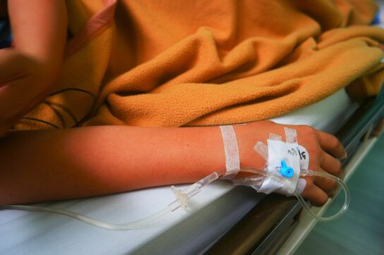 Close up of someones right arm with an IV line in their hand depicting biologic medication which can be very expensive