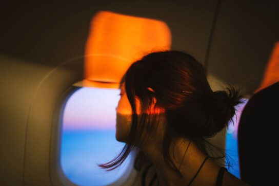 An adult looking out of an airplane window, hoping to avoid traveler's stomach.