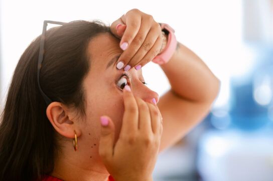 Person pulling back their lower and upper eyelid to put a contact lens in.