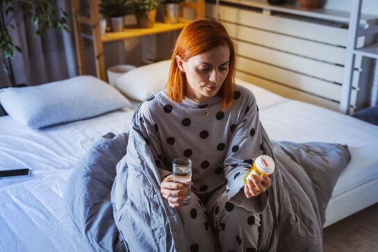An adult sitting in bed, looking at a bottle of risperidone to be taken at night.