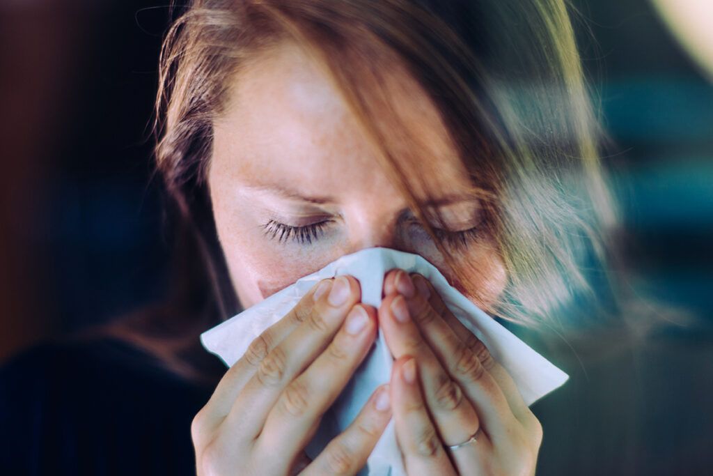 An adult blowing their nose into a tissue. They may have COVID-19 or a cold.