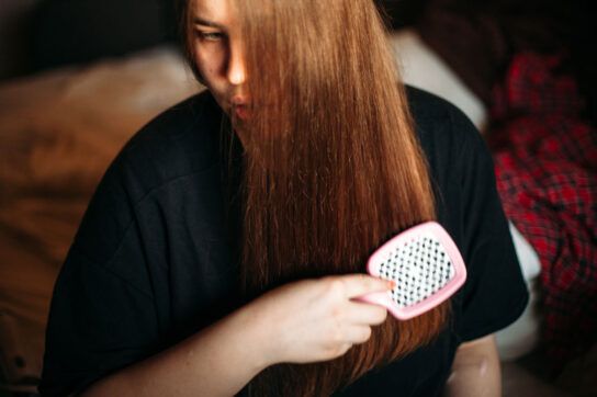 Adult female brushing long hair over half of their face as they could be wondering if there is a link between depression and hair loss