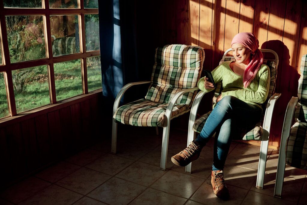 An adult wearing a headscarf looking at their phone, waiting to receive chemotherapy.