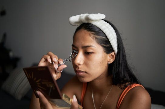 A young woman curling her eyelashes, thinking about what causes a stye.