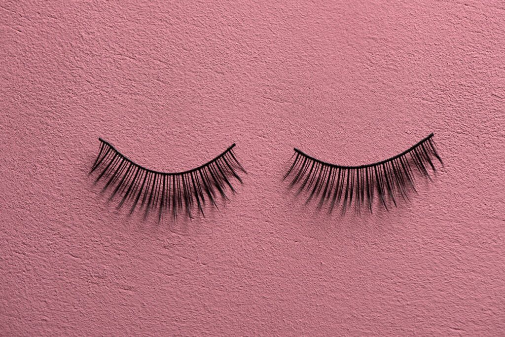 A pair of fake lashes on a pink surface.