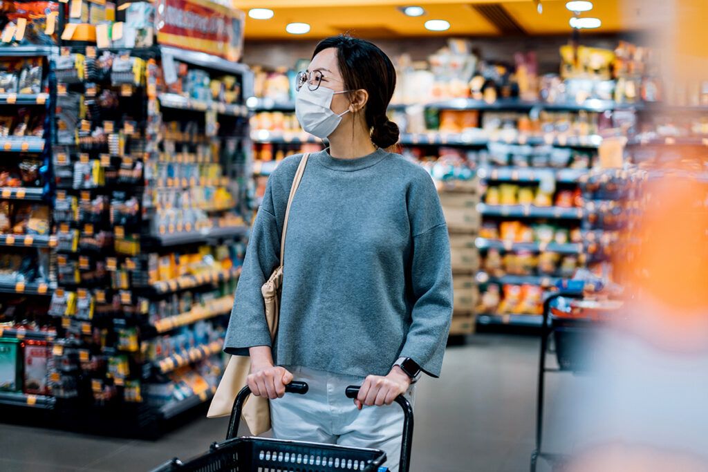 An adult grocery shopping while wearing a face covering to protect against COVID-19 reinfection.