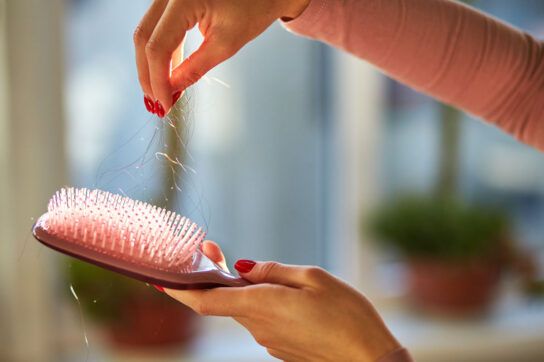 Person pulling loose hair out of a pink paddle brush.
