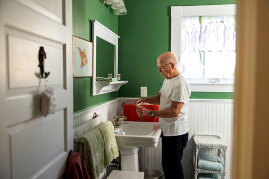 Bald man in green painted home bathroom taking medication from pill bottle