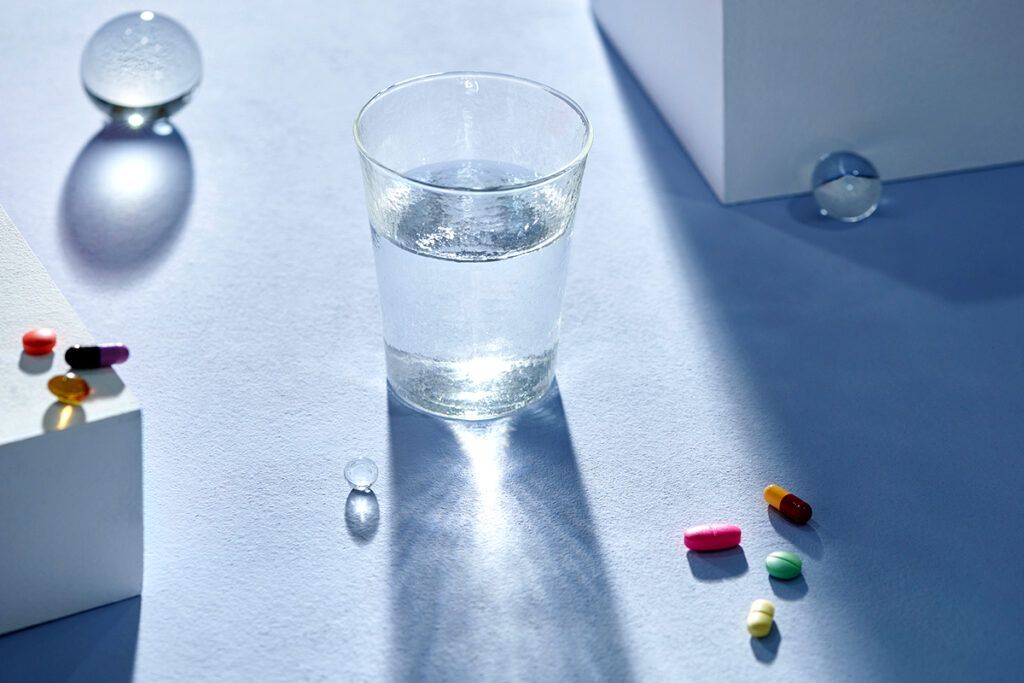 A glass of water on a surface surrounded by several pills.