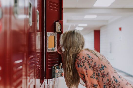 Female high school student with their back to the camera looking at a mirror on the inside of their locker door possibly wondering why do I sweat so much at school