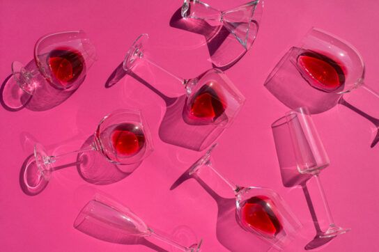 Different types of glasses with wine in them arranged on a pink background.