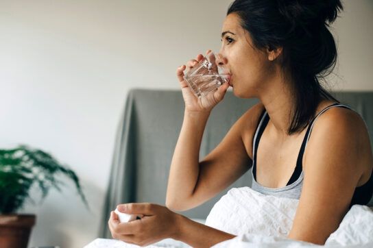Woman sitting up in bed drinking water to take medication