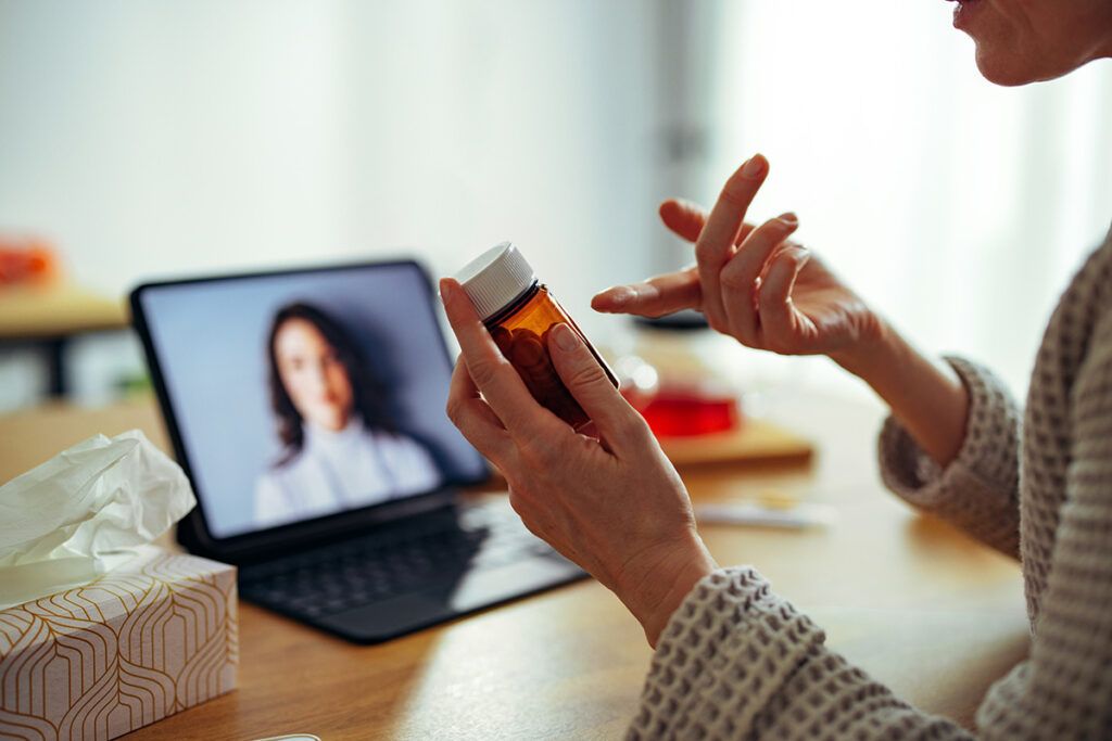 An adult on a video call with a healthcare professional gesturing to a bottle of yeast infection medication.