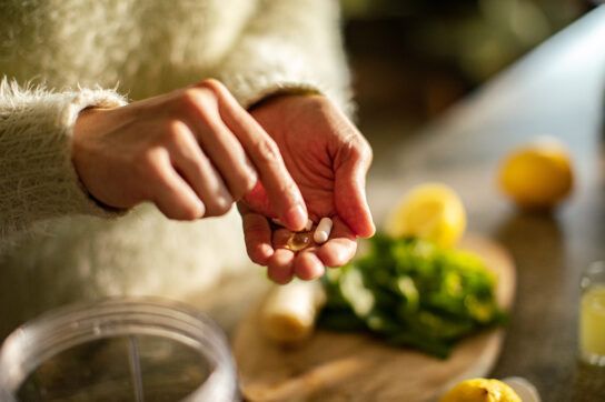 Woman's hands holding small assortment of pills above food prep area in kitchen