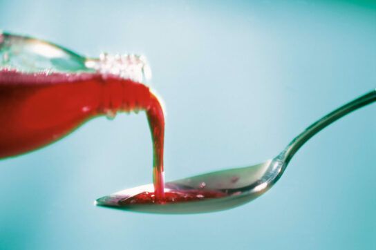 Red cough syrup being pour into silver teaspoon