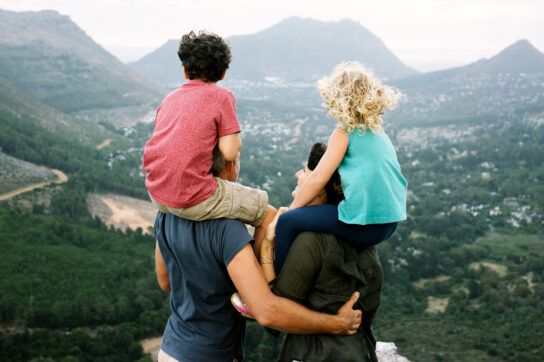 Parents with small children on their shoulders look out at mountain landscape