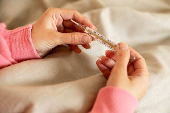 Adult holding a thermometer, image focused on their hands. They could be looking at the reading and wondering if body temperature is the same as blood temperature