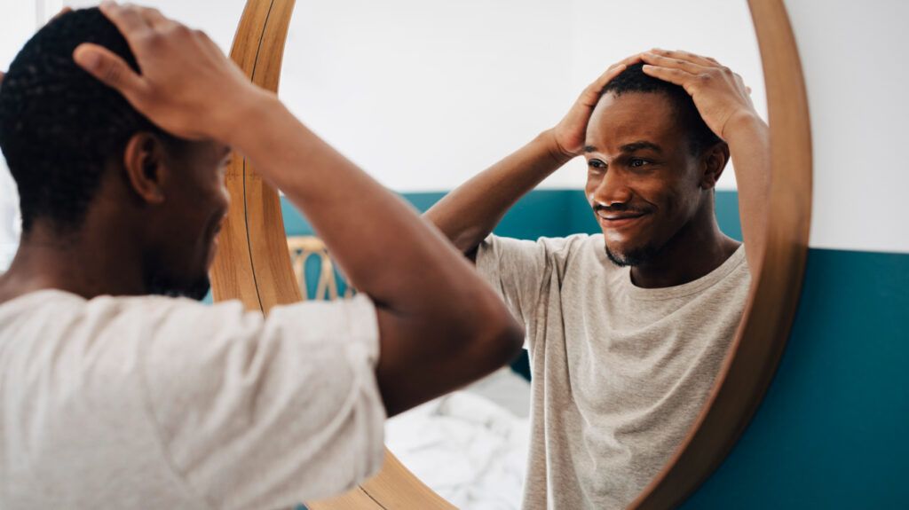 A man standing in the mirror with his hands going through his hair