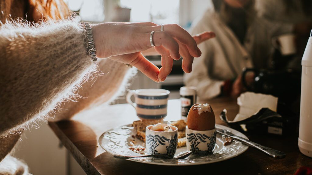a person's hand sprinkling salt over an egg on their breakfast plat