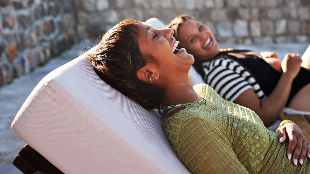 A woman wearing a green shirt, reclining in a chair outdoors, laughing with her friend, enjoying herself after healing from a fungal infection
