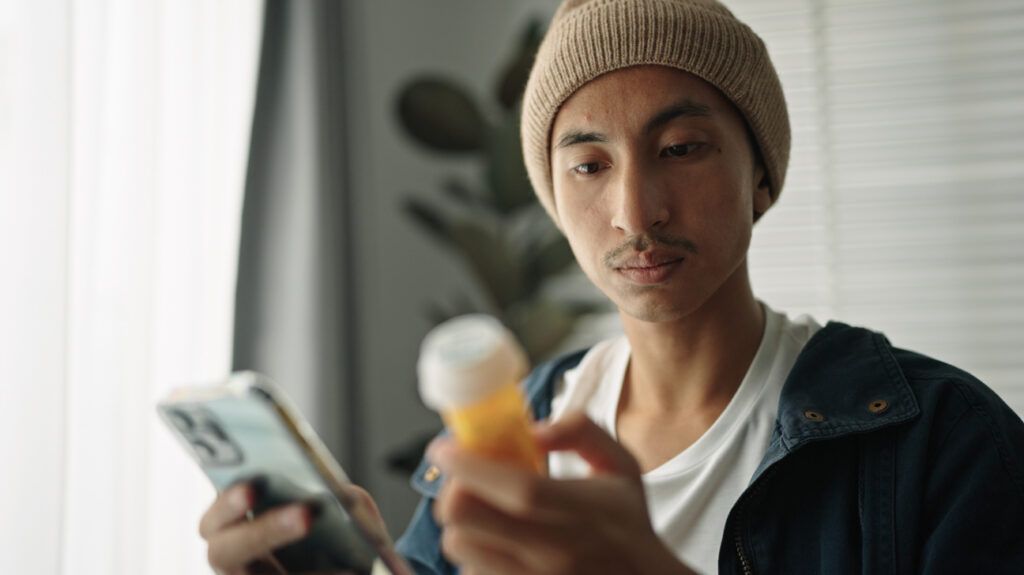 A person looking at a pill bottle while looking up information on prescription refills without a doctor on their phone.