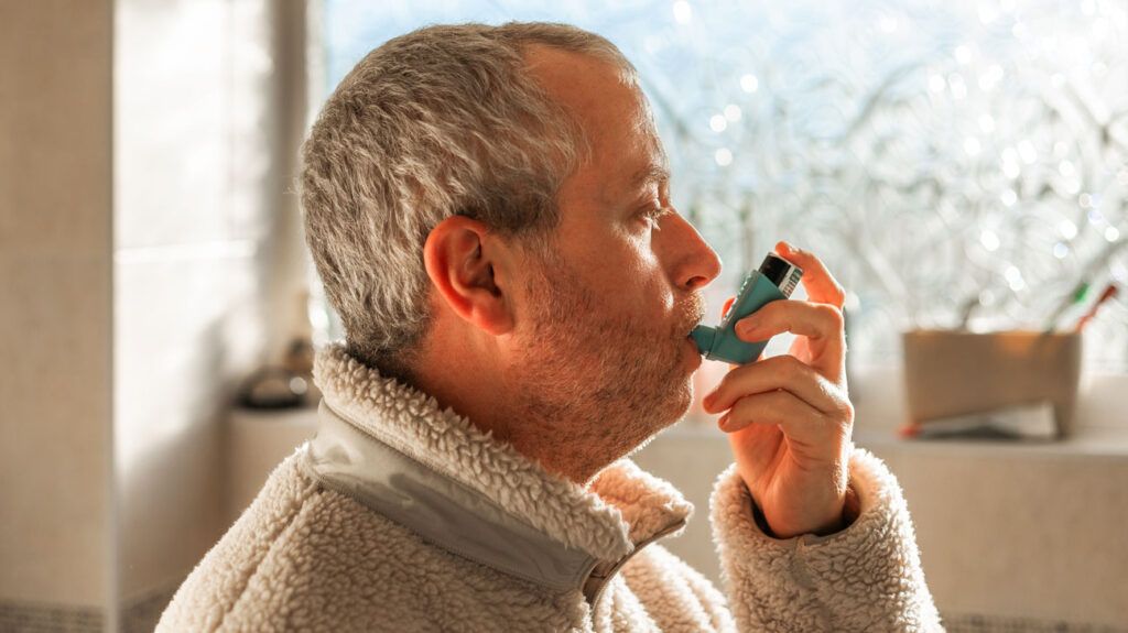 Profile view of an older man using an albuterol inhaler